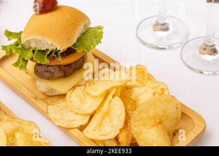 Eine obere Nahaufnahme eines Burgers und Chips auf der Holzplatte auf dem weißen Hintergrund Stockfoto