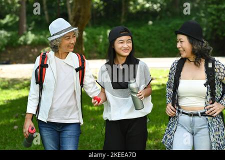 Zwei glückliche ältere Freunde und ein Mädchen im Teenageralter, die im Park spazieren gehen und miteinander reden Stockfoto