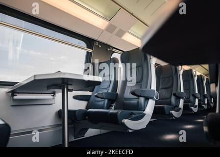 Blick auf den Tisch und die leeren Sitze am Fenster. Innenraum des modernen Hochgeschwindigkeitszuges. Bequemer Bahnverkehr in der Stadt. Stockfoto