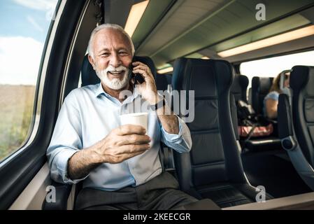 Lächelnder Geschäftsmann im Gespräch auf dem Smartphone. Männlicher Unternehmer hat Kaffee, während er in der U-Bahn sitzt. Während der Busi trägt er Formalien Stockfoto