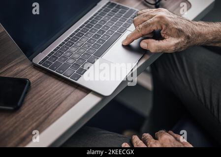 Nahaufnahme des männlichen Senior-Profis beim Scrollen auf dem Laptop am Tisch. Geschäftsmann arbeitet in der U-Bahn oder im Intercity-Zug. Er verwendet Wireless Stockfoto