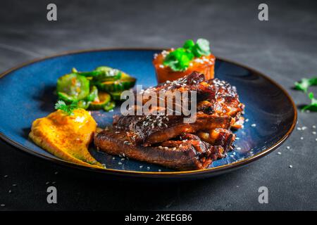 Schmackhafte und würzige geröstete Rippchen mit Gemüse und Sesam. Rippchen mit Kartoffelpüree als Fusion Cuisine. Stockfoto