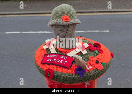 Leigh on Sea, Großbritannien. November 2022. Dekorative Häkelhülle über einem öffentlichen Postkasten in Leigh-on-Sea zum Gedenken an den Gedenktag. Mit einer Helm-Soldatenfigur, rotem Mohn, zwei Holzkreuzen, einem kleinen gestrickten Hund und einem zentralen Patch mit der Aufschrift „LEST WE FORGET“. Eine herzliche Hommage an gefallene Militärs durch kommunales Handwerk. Penelope Barritt/Alamy Live News Stockfoto