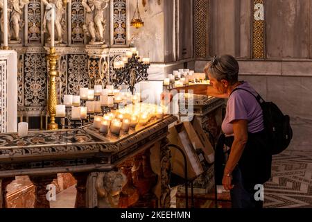 Eine Frau, die eine Kerze in der Kathedrale von Monreale, Palermo, Sizilien, Italien, beleuchtet. Stockfoto