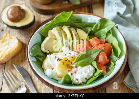 Ketogene, Keto- oder Paläodiät. Köstliches Frühstück oder eine Schüssel mit gesalzenem Lachsfisch, Avocado, gekochtem Ei und Spinat auf einem rustikalen Tisch. Stockfoto