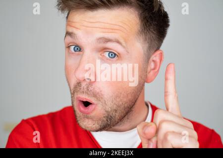 Zufriedener junger Mann zeigt Zeigefinger nach oben und gibt Ratschläge oder Empfehlungen Stockfoto