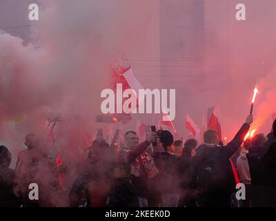 Menschen feiern den polnischen Unabhängigkeitstag, den 11. November. Menge mit polnischen Fahnen, die in Rauch gehüllt sind. Einige halten Fackeln fest. Stockfoto