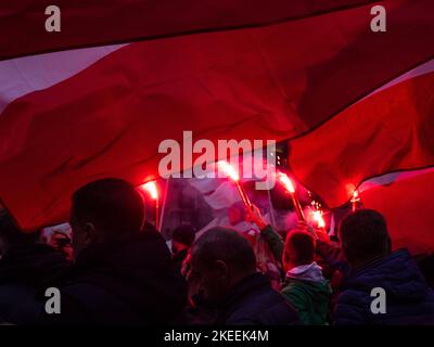 Menschen mit Fackeln und Fahnen während des Unabhängigkeitstages. Polen, 11. November 2022. unabhängigkeitsmarsch. Abend, helle Flammen von Fackeln, Rauch. Stockfoto