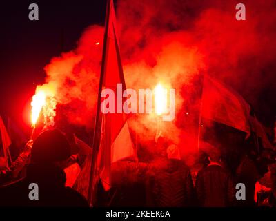 Menschen mit Fackeln und Fahnen während des Unabhängigkeitstages. Polen, 11. November 2022. unabhängigkeitsmarsch. Abend, helle Flammen von Fackeln, Rauch. Stockfoto