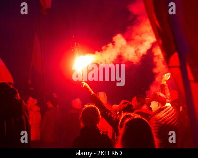 Menschen mit Fackeln und Fahnen während des Unabhängigkeitstages. Polen, 11. November 2022. unabhängigkeitsmarsch. Abend, helle Flammen von Fackeln, Rauch. Stockfoto