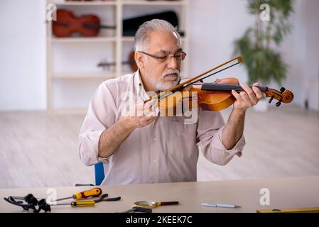 Ein alter Mechaniker repariert Musikinstrumente in der Werkstatt Stockfoto