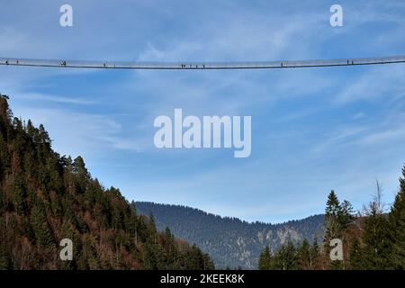 Waghalsige Touristen, die über die Hängebrücke Highline179 mit blauem Himmel in Reutte, Tirol, Österreich, laufen Stockfoto