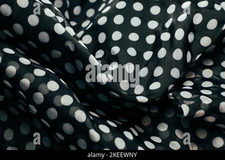 Geraffte und gefaltete Textur aus schwarz-weißem Polka-Punkt bedrucktem Stoff. Wellen und Falten bilden eine wellige schwarze Textur. Nahtloses Stoffmuster. Stockfoto