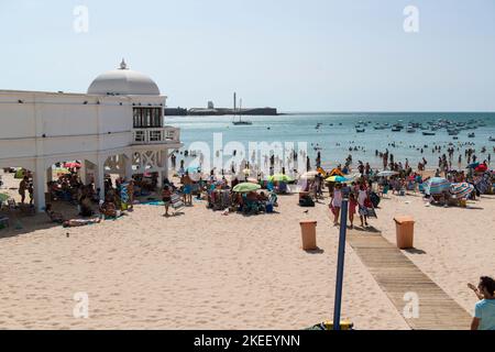 Sonnenanbeter an der Playa de la Caleta in der Nähe des Balneario de la Palma in Cádáiz, Andalusien, Spanien. Stockfoto