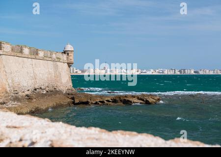 Die Mauern von Castillo de San Sebastián, Cádiz, Spanien, befinden sich auf einer kleinen Insel, die von der Hauptstadt getrennt ist und im Hintergrund sichtbar ist. Stockfoto