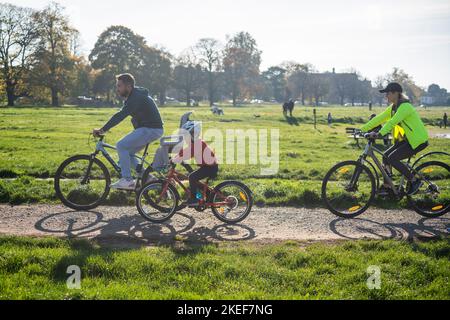 London, Großbritannien. 12. November 2022. Eine Familie, die im für die Saison unheimlich warmen Sonnenschein auf dem Wimbledon Common im Südwesten Londons radelt, da die Temperaturen dieses Wochenende voraussichtlich 17celsius erreichen werden. Kredit: amer ghazzal/Alamy Live Nachrichten Stockfoto