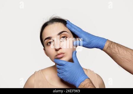 Eine Frau, die ihre Augenbrauen von einem professionellen Make-up-Künstler im Hintergrund gemacht bekommt, ist die Hand eines Mannes, der blaue Handschuhe trägt Stockfoto