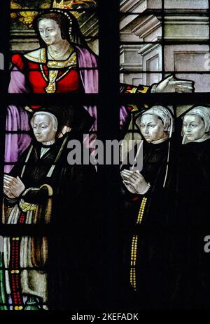 Weibliche Mitglieder der Familie einer Stifterin aus Buntglas knien im Gebet unter Szenen aus dem Leben der Jungfrau Maria: Vor der Reformation Buntglas von 1555 von Lambert van Noort und Digman Meynaert in der Lady Chapel of the Oude Kerk or Old Church in Ouderkerksplein, Amsterdam, Niederlande, das eine Welle von Ikonoklasmus überlebte, ausgelöst durch die niederländische Reformation. Stockfoto