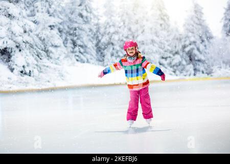 Schlittschuhlaufen auf natürlichem Eis am verschneiten Wintertag. Kinder mit Schlittschuhe. Kleines Mädchen, das im verschneiten Park auf einem gefrorenen See Schlittschuh laufen kann. Schnee und Winterspaß. Gesund raus Stockfoto