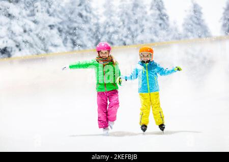 Schlittschuhlaufen auf natürlichem Eis am verschneiten Wintertag. Kinder mit Schlittschuhe. Kleine Mädchen und Jungen beim Schlittschuhlaufen auf gefrorenem See im verschneiten Park. Schnee Winter Spaß. Gesund Stockfoto