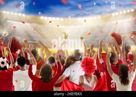 Fußballfan im Stadion in rot-weißem Hemd. Fröhliche Fans auf dem Fußballfeld, die das siegreiche Mannschaftsspiel beobachten. Gruppe von Unterstützern Stockfoto