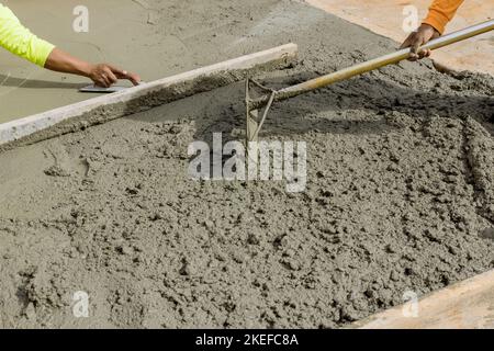 Die Arbeiter gießen Zement auf die Seite des Hauses, um einen neuen Bürgersteig zu schaffen Stockfoto