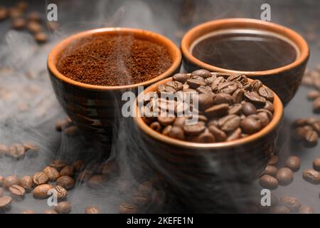 Tassen Kaffee unter ausgewählten und kalibrierten Arabica-Kaffeebohnen, verteilt auf schwarzem Hintergrund, drei aromatische Tassen Kaffee in einem Paar. Stockfoto