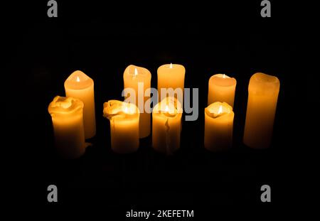 Eine Gruppe von neun brennenden Wachskerzen mit schwarzem Hintergrund Stockfoto