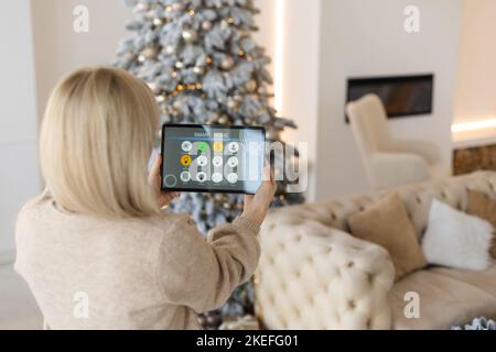 Junge Frau verwendet Anwendung in seinem Smart Home zu Weihnachten Stockfoto