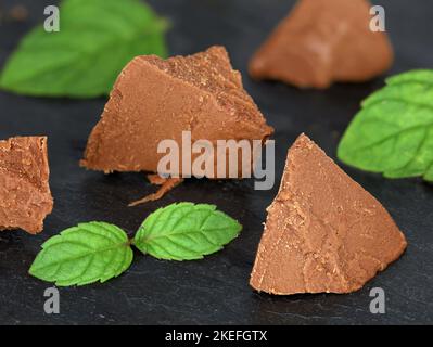 Süße Schokoladen-Haselnuss-Nougatstücke mit Minzblättern isoliert auf schwarzem Schieferbrett, als Backzutat oder süßer Aufstrich Stockfoto