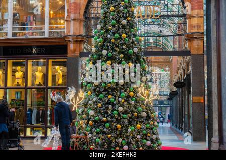 In einer Einkaufspassage im Victoria Quarter, Leeds, England, stand ein Einkäufer neben einem hohen Weihnachtsbaum, der mit großen Kugeln dekoriert war. Stockfoto