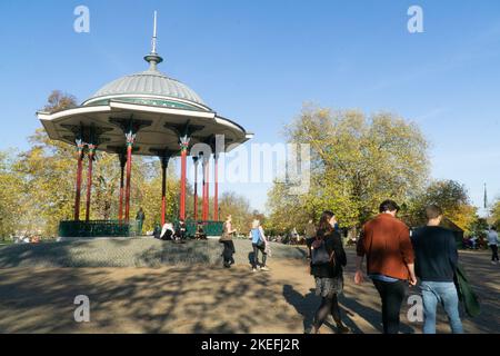 Wetter in Großbritannien, 12. November 2022: In Clapham, im Süden Londons, ist das ungewöhnlich milde Wetter und die strahlende Sonne ein Genuss für Menschen in Cafés im Freien, für Hundewanderer, Kinderwagen und Radfahrer auf Clapham Common und gibt schöne Reflexionen in den Teichen. Anna Watson/Alamy Live News Stockfoto