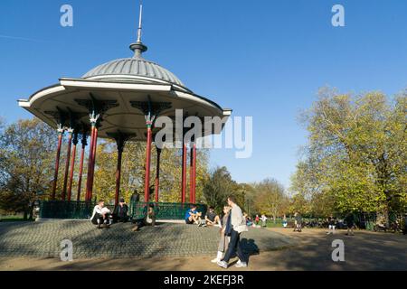 Wetter in Großbritannien, 12. November 2022: In Clapham, im Süden Londons, ist das ungewöhnlich milde Wetter und die strahlende Sonne ein Genuss für Menschen in Cafés im Freien, für Hundewanderer, Kinderwagen und Radfahrer auf Clapham Common und gibt schöne Reflexionen in den Teichen. Anna Watson/Alamy Live News Stockfoto