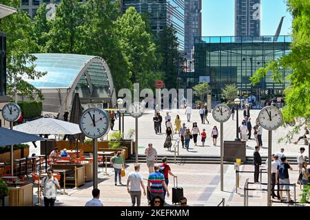 London, England - 2022. Juni: Besucher und Büroangestellte gehen in Canary Wharf an stehenden Uhren vorbei Stockfoto