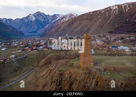 Evening aerial view of an old miltary stone tower and traditional village in the back in kazbegi region, caucasus, georgia Stockfoto