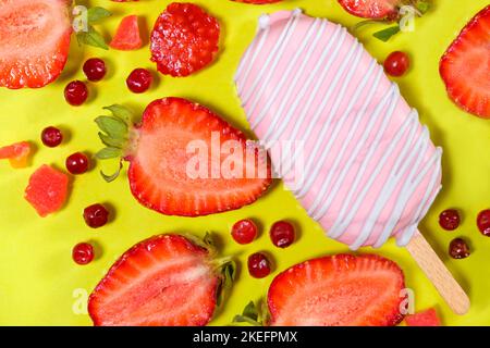 Rosafarbenes Eis auf einem Stock mit Erdbeeren und roten Preiselbeeren auf gelbem Hintergrund. Stockfoto