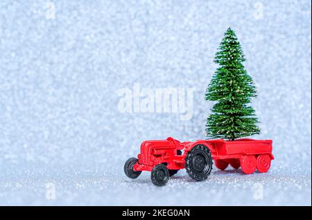 Spielzeug roten Traktor mit einem Miniatur-Weihnachtsbaum in der Kutsche isoliert auf einem funkelnden Hintergrund platziert. Neujahr Bäume Landwirtschaft und Lieferung. Stockfoto