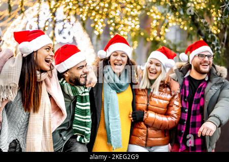 Junge Freunde Gruppe unter Weihnachtsbaum Dekorationen zu Fuß - Winter Lifestyle-Konzept mit trendigen glücklichen Menschen tragen roten santa Hüte, während mit Stockfoto