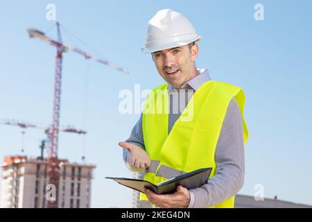 Professioneller Baumeister, der mit einem Notebook vor der Baustelle steht Stockfoto