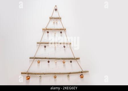 An einer weißen Wand ein Baum aus natürlichen Materialien, Treibholz. Kreative Dekorationen in Form eines Weihnachtsbaums, mit goldenen Kugeln. Skandinavisch, r Stockfoto