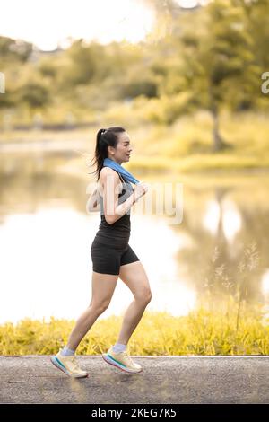 Eine flache Aufnahme einer südostasiatischen Frau in schwarzer Sportkleidung, die draußen läuft Stockfoto