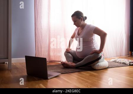 Junge Schwangere praktiziert zu Hause Yoga Stockfoto