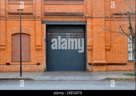 Rote Ziegelwand mit automatischen Metallrolltoren, die in der Fabrik, im Lager, in der Garage und im Industrielager verwendet werden. Stockfoto