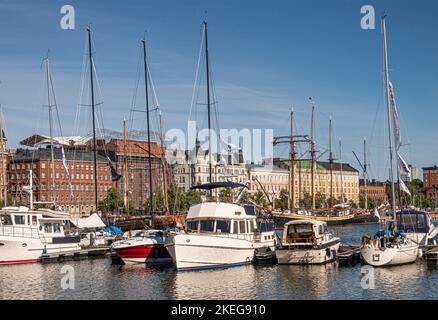 Helsinki, Finnland - 20. Juli 2022: Hafen Pohjoissatama. Reihe von kleineren, meist weißen Motorbooten, die am Pier angedockt sind. Fassaden hoher Bürogebäude in Stockfoto