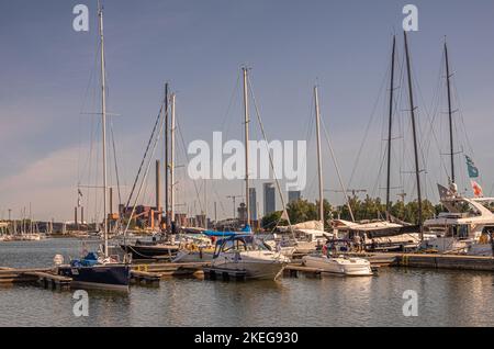 Helsinki, Finnland - 20. Juli 2022: Hafen Pohjoissatama. Reihe von Segel-und. Motorboote angedockt am Pier. Hanasaari Power Plant Schornsteine und Wohnhäuser Stockfoto