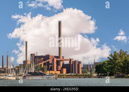 Helsinki, Finnland - 20. Juli 2022: Hafen Pohjoissatama. Kraftwerk Hanasaari aus rotem Stein mit hohen Schornsteinen vor blauer Wolkenlandschaft. Schiff in Port wa Stockfoto