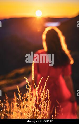 Beschreibung: Schöne braune Frau in rotem Kleid, die die sonnige Abendstimmung auf dem Pico do Ariero genießt. Verade do Pico Ruivo, Madeira Stockfoto