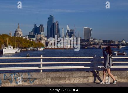 London, Großbritannien. 12.. November 2022. Eine Frau geht an einem ungewöhnlich warmen Novembertag, an dem die Temperaturen in der Hauptstadt steigen, an der Waterloo Bridge vorbei an der Skyline der City of London. (Bild: © Vuk Valcic/SOPA Images via ZUMA Press Wire) Stockfoto