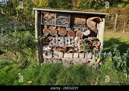 Insektenhotel mit Steinen, alten Fliesen, gebohrten Löchern in Baumstämmen, Rinde, Bambus, Lehm und mit Unterschlupf für Schmetterlinge. In einem holländischen Garten im Herbst Stockfoto