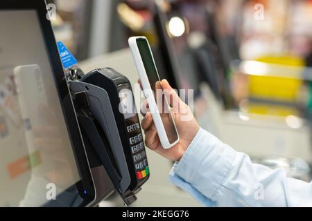 Closeup Woman Counter Elektronische Bezahlung kaufen Supermarkt Smartphone Female Hand mit Mobiltelefon in Bezahlung für Einkäufe in Geschäften Kontaktloses NFC Terminal Closeup Kartenleser. Stockfoto